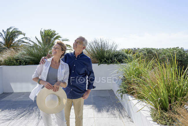 Feliz pareja de ancianos mirando hacia arriba mientras está de pie en la terraza en el jardín - foto de stock