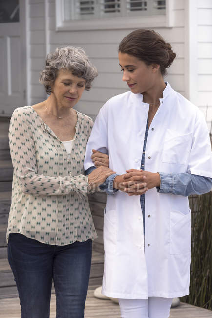 Жіноча медсестра допомагає усміхненій старшій жінці в будинку престарілих — стокове фото