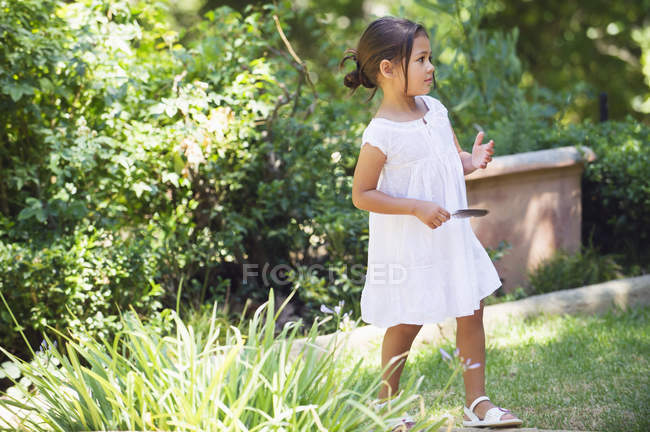 Kleines Mädchen im weißen Sommerkleid, das im Sommergarten spaziert — Stockfoto