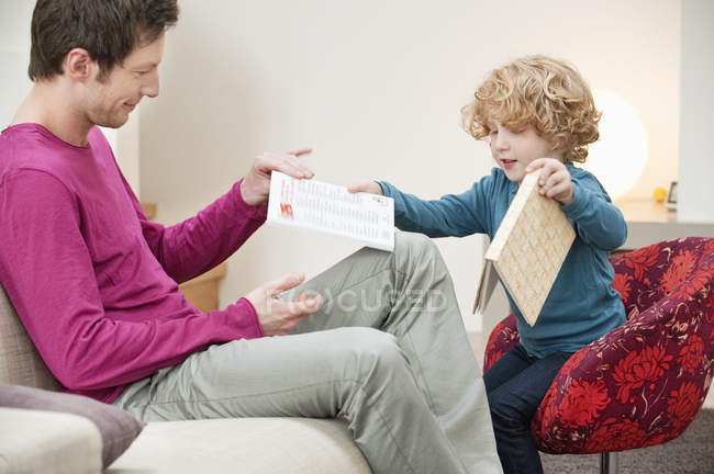 Hombre dando libro a su pequeño hijo en el sofá en casa - foto de stock