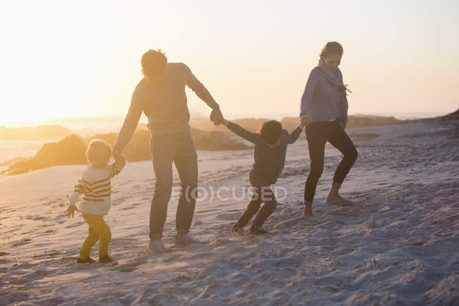 Pais com crianças andando na praia de mãos dadas ao pôr do sol — Fotografia de Stock