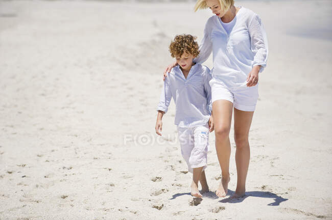 Mujer caminando con su hijo en la playa - foto de stock