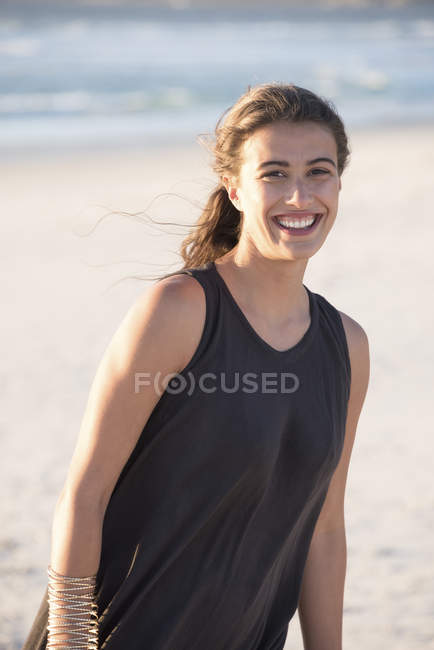 Lächelnde junge Frau in schwarzem Top steht am Strand — Stockfoto