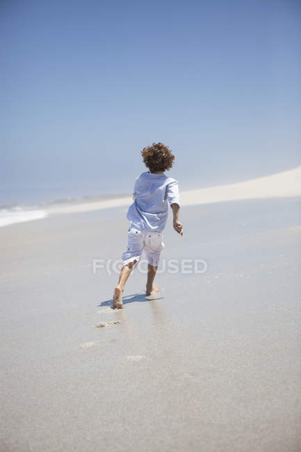 Visão traseira de um menino correndo na praia de areia — Fotografia de Stock
