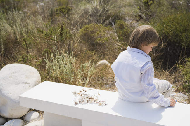 Vista trasera del niño soñador sentado en un banco de hormigón al aire libre - foto de stock