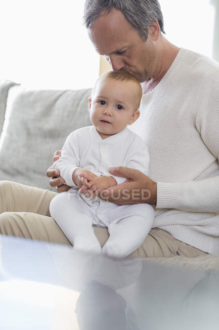 Father kissing cute baby daughter on sofa in living room — Stock Photo
