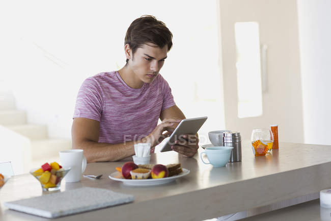 Jovem usando tablet digital na mesa da cozinha — Fotografia de Stock