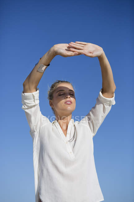 Jeune femme debout les yeux fermés contre le ciel bleu — Photo de stock