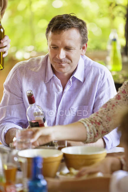 Uomo maturo guardando bottiglia di vino mentre seduto al tavolo terrazza — Foto stock
