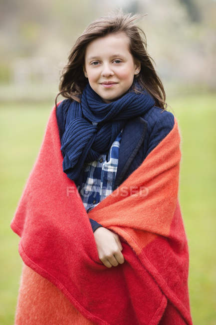 Retrato de niña sonriente envuelta en manta de pie en el campo sobre fondo borroso - foto de stock