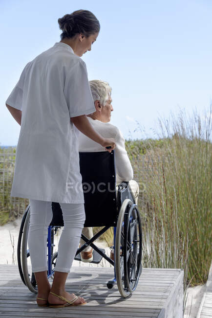 Female nurse assisting senior man in wheelchair outdoors — Stock Photo