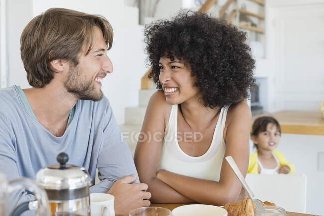 Paar lächelt am Esstisch mit Tochter im Hintergrund — Stockfoto