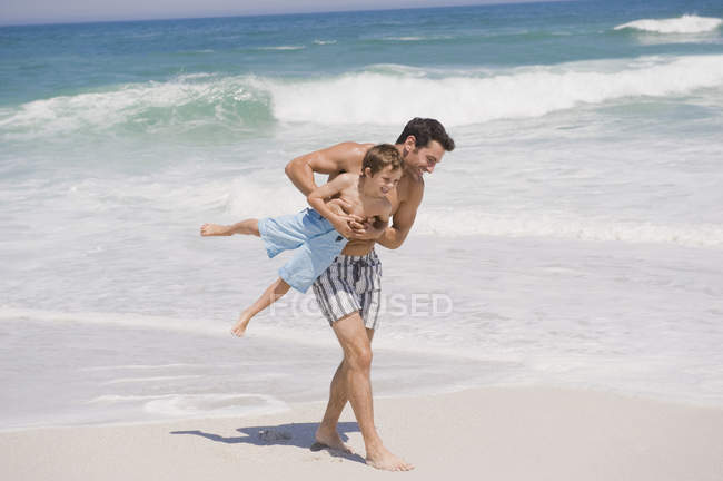 Homme gai jouant avec son fils sur la plage de sable — Photo de stock