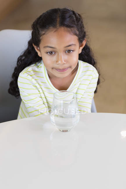 Маленька дівчинка сидить зі склянкою води за столом — стокове фото