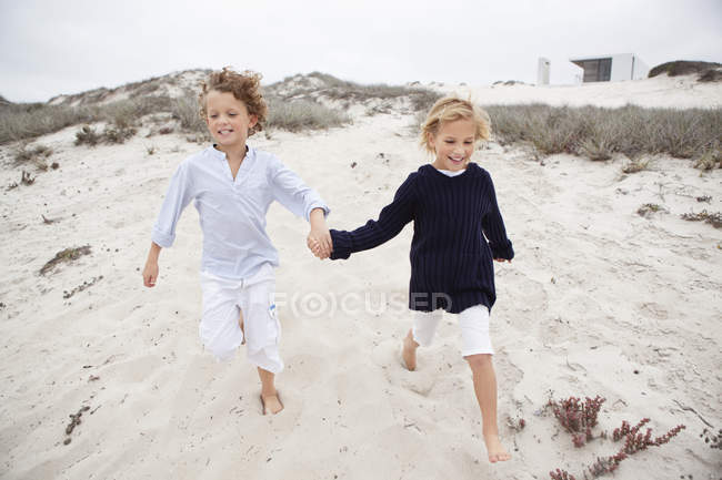 Мальчик с сестрой держатся за руки и бегают по песку — стоковое фото