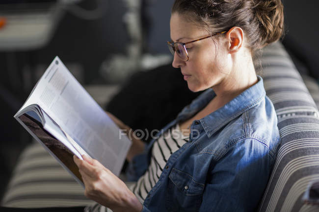 Крупный план задумчивой женщины читающей журнал, сидящей на диване — стоковое фото