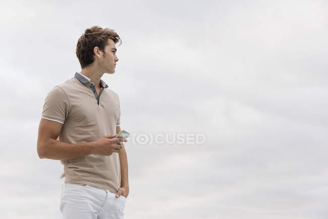 Junger Mann hält Smartphone unter wolkenverhangenem Himmel — Stockfoto