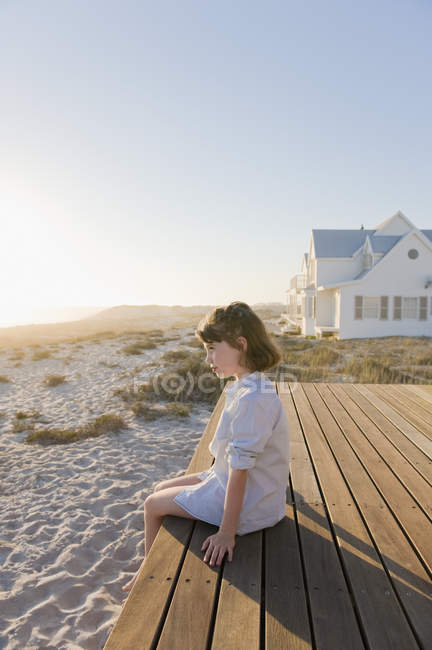 Verträumtes kleines Mädchen sitzt auf der Strandpromenade am Sandstrand — Stockfoto