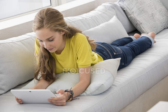 Девочка-подросток с помощью цифрового планшета на диване дома — стоковое фото