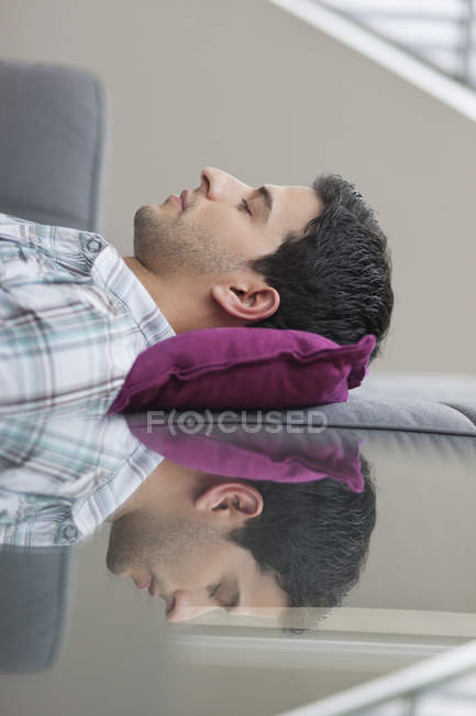 Розслаблений чоловік лежить на дивані з відображенням на скляному столі — стокове фото