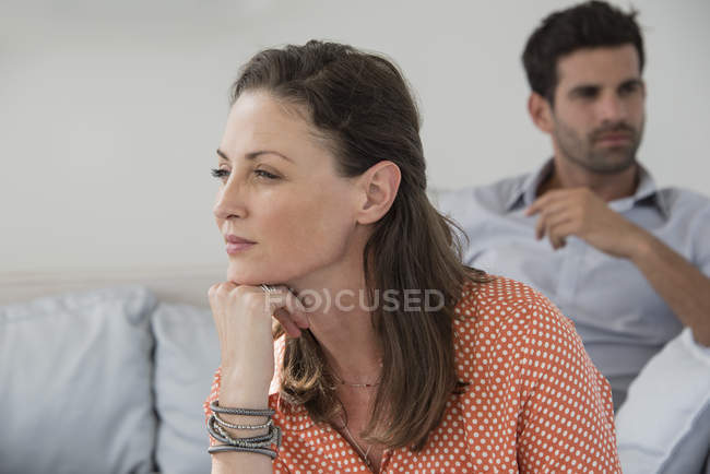 Close-up de mulher pensativa sentada no sofá com o marido no fundo — Fotografia de Stock