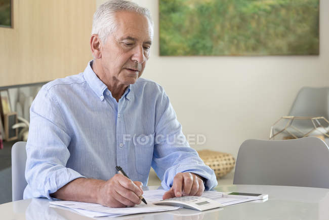 Старший использует калькулятор во время бумажной работы дома — стоковое фото