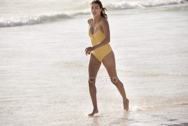 Young slim woman in yellow swimsuit running on beach — Stock Photo
