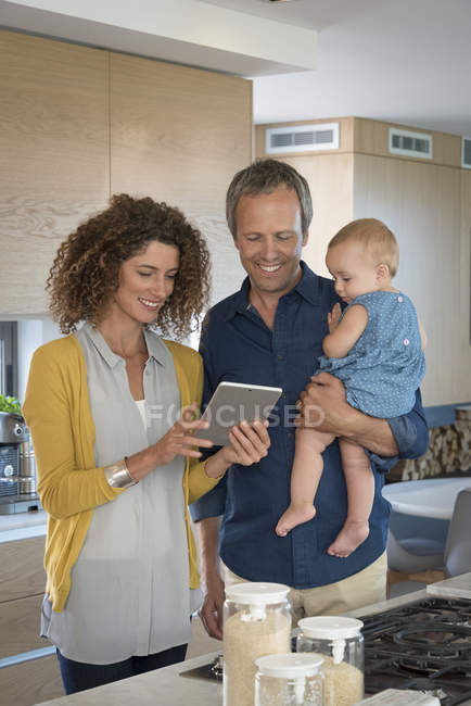 Couple using digital tablet with baby daughter in kitchen — Stock Photo