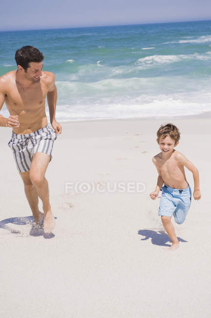 Веселый мужчина бегает с сыном на песчаном пляже — стоковое фото