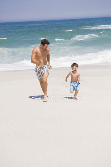 Fröhlicher Mann läuft mit Sohn am Sandstrand — Stockfoto