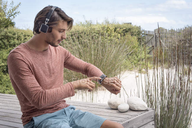 Young man using checking smartwatch and listening to music with headphones in garden — Stock Photo