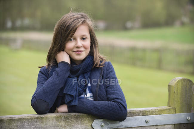 Retrato de menina sorrindo sorrindo inclinando-se sobre cerca no campo — Fotografia de Stock