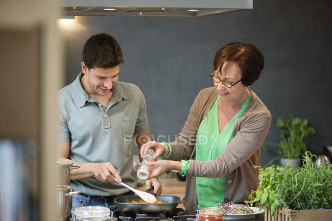 Mujer ayudando a su hijo a cocinar comida - foto de stock