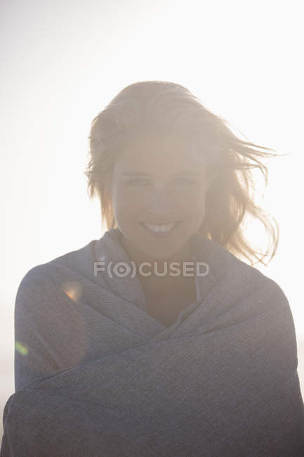 Smiling young woman wrapped in shawl standing in back light — Stock Photo