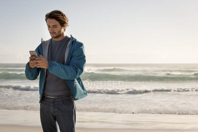 Jeune homme utilisant un téléphone mobile sur la plage — Photo de stock
