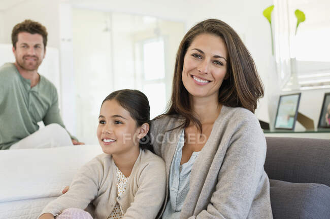 Усміхнена жінка сидить зі своєю дочкою і чоловіком на задньому плані — стокове фото