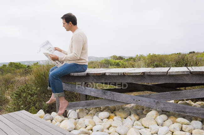 Homem sentado no calçadão na natureza e lendo um jornal — Fotografia de Stock