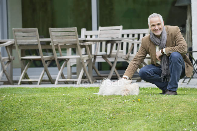 Улыбчивый взрослый мужчина играет с собакой в саду — стоковое фото