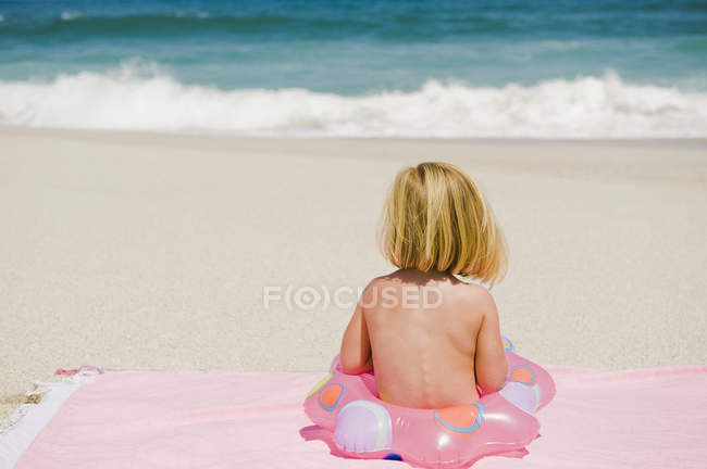 Menina sentada com anel inflável na praia de areia — Fotografia de Stock