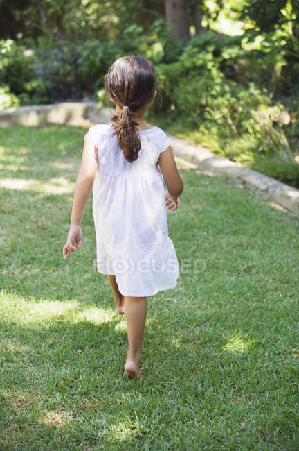 Visão traseira da menina no vestido de verão branco andando no jardim ensolarado — Fotografia de Stock