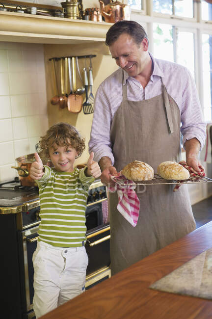 Niño mostrando pulgares hacia arriba signo con el padre sosteniendo panes horneados - foto de stock