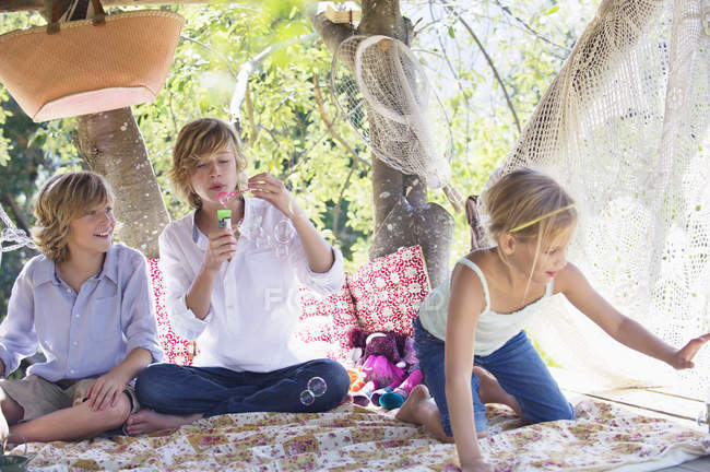 Crianças soprando varinha de bolha na casa da árvore — Fotografia de Stock