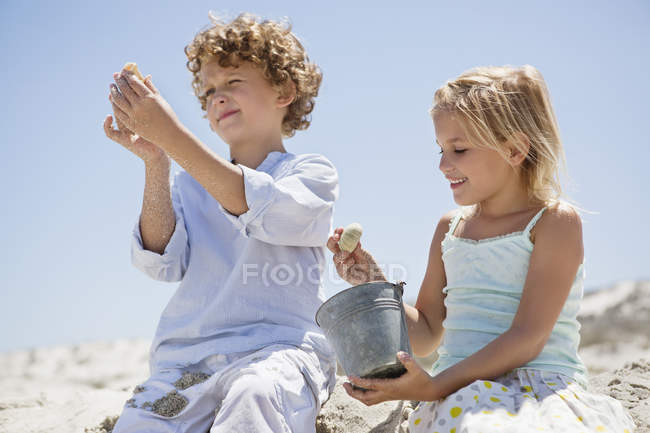 Frère et sœur regardant des coquillages sur une plage de sable — Photo de stock