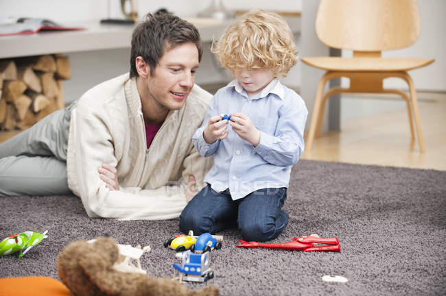Uomo che gioca con il piccolo figlio sul tappeto a casa — Foto stock