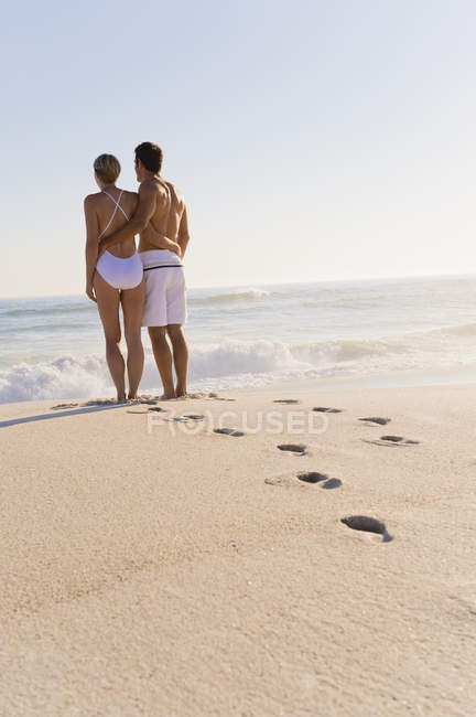 Відбитки слідів на піщаному пляжі з парою, що стоять на фоні і дивляться на вигляд — стокове фото