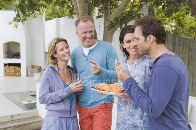 Cuatro amigos comiendo frutas y divirtiéndose - foto de stock