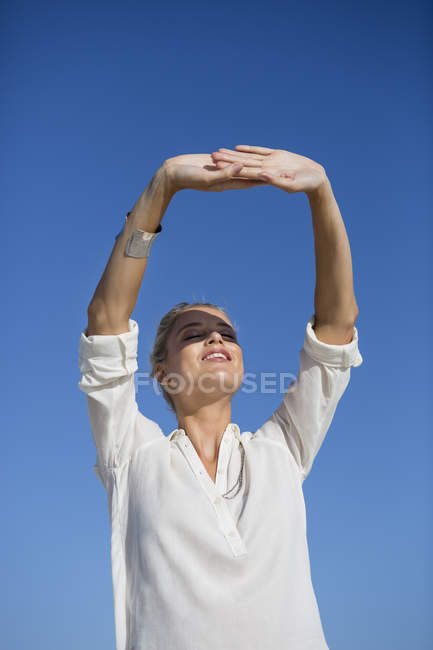 Молодая женщина стоит с закрытыми глазами на фоне голубого неба — стоковое фото