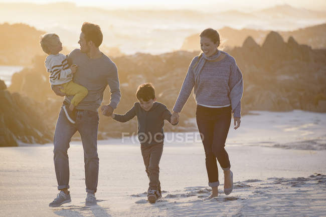Feliz joven familia caminando en la playa al atardecer - foto de stock