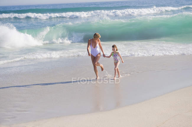 Mulher correndo na praia de areia com a filha — Fotografia de Stock