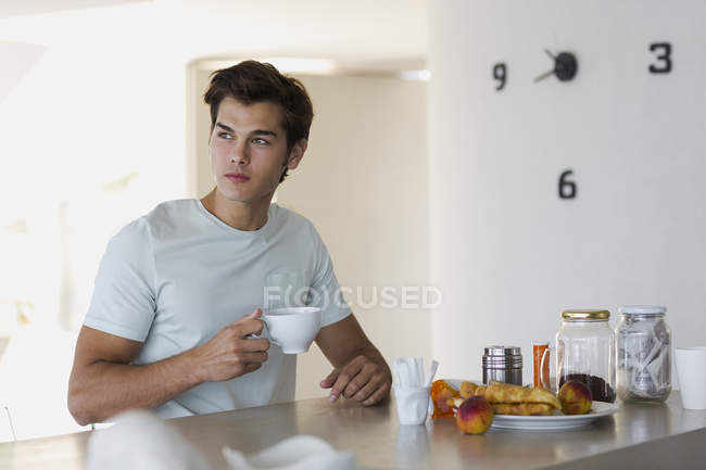 Close-up de jovem pensativo bebendo café na mesa na cozinha — Fotografia de Stock